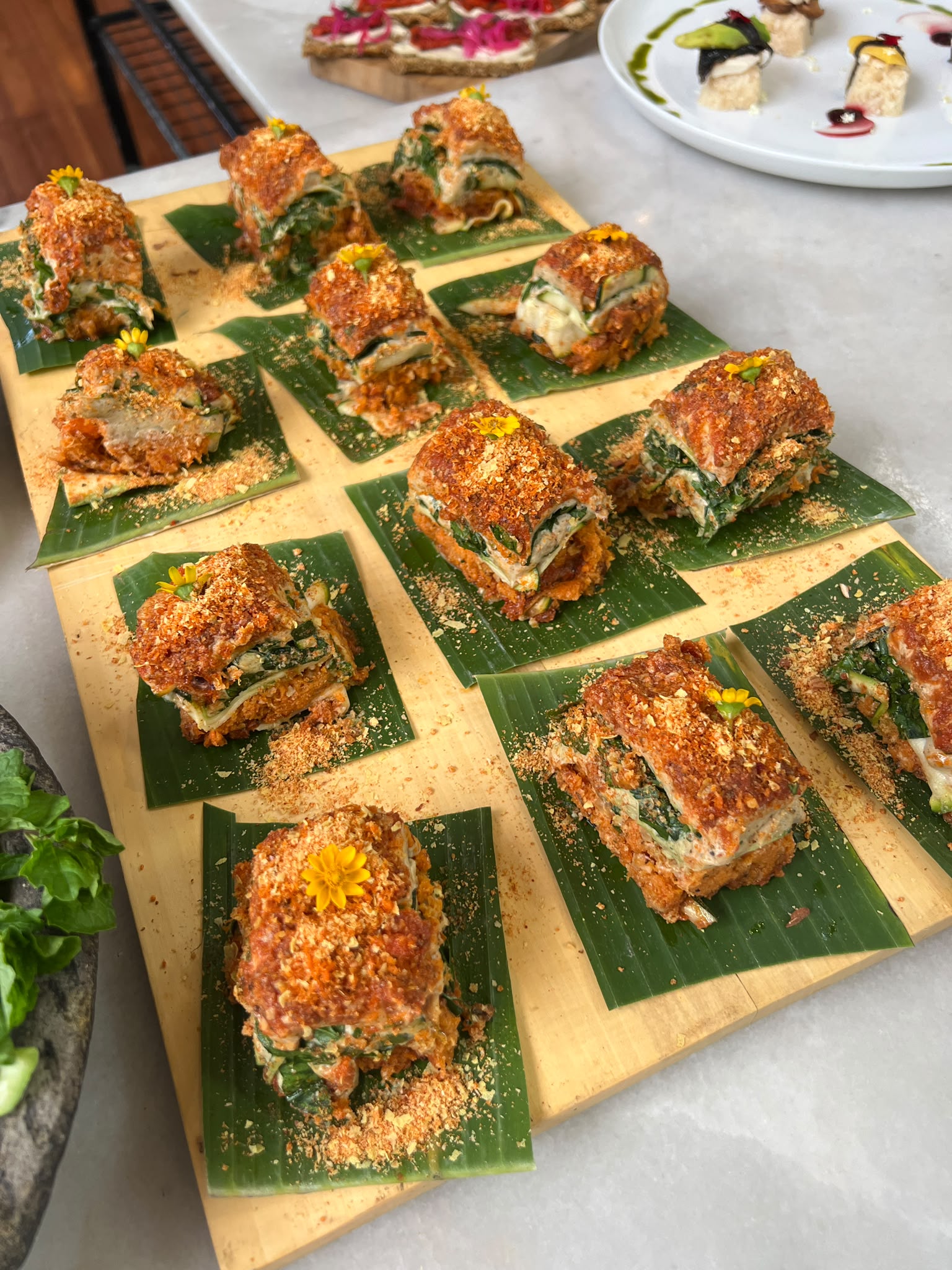 Raw vegan lasagna bites with edible flowers served on banana leaves